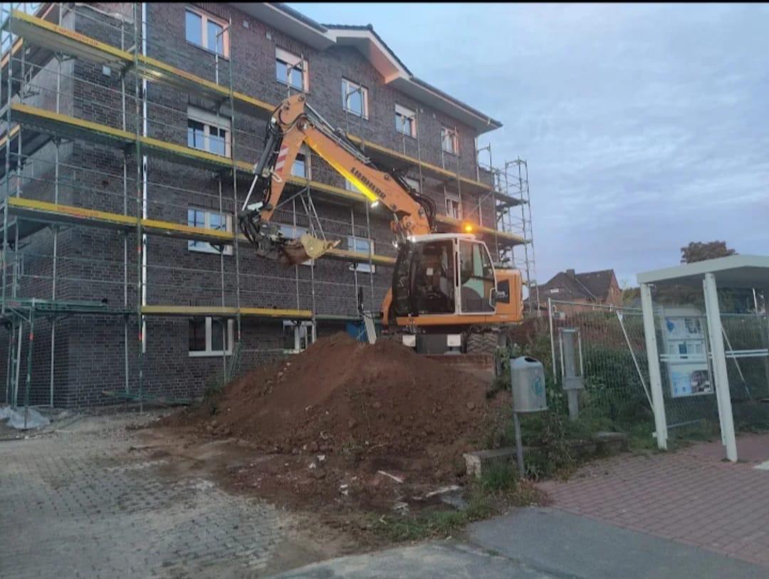 Bagger vor einem eingerüsteten Mehrfamilienhaus